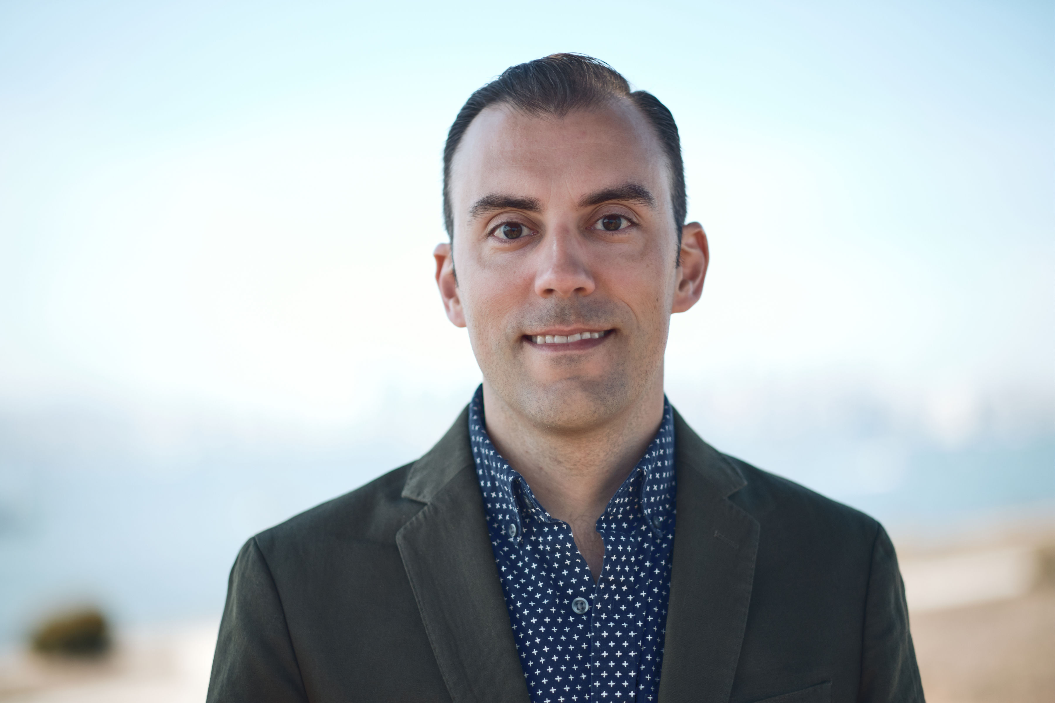 Grant Shellen in a navy blue shirt and olive green blazer with the skyline in the background